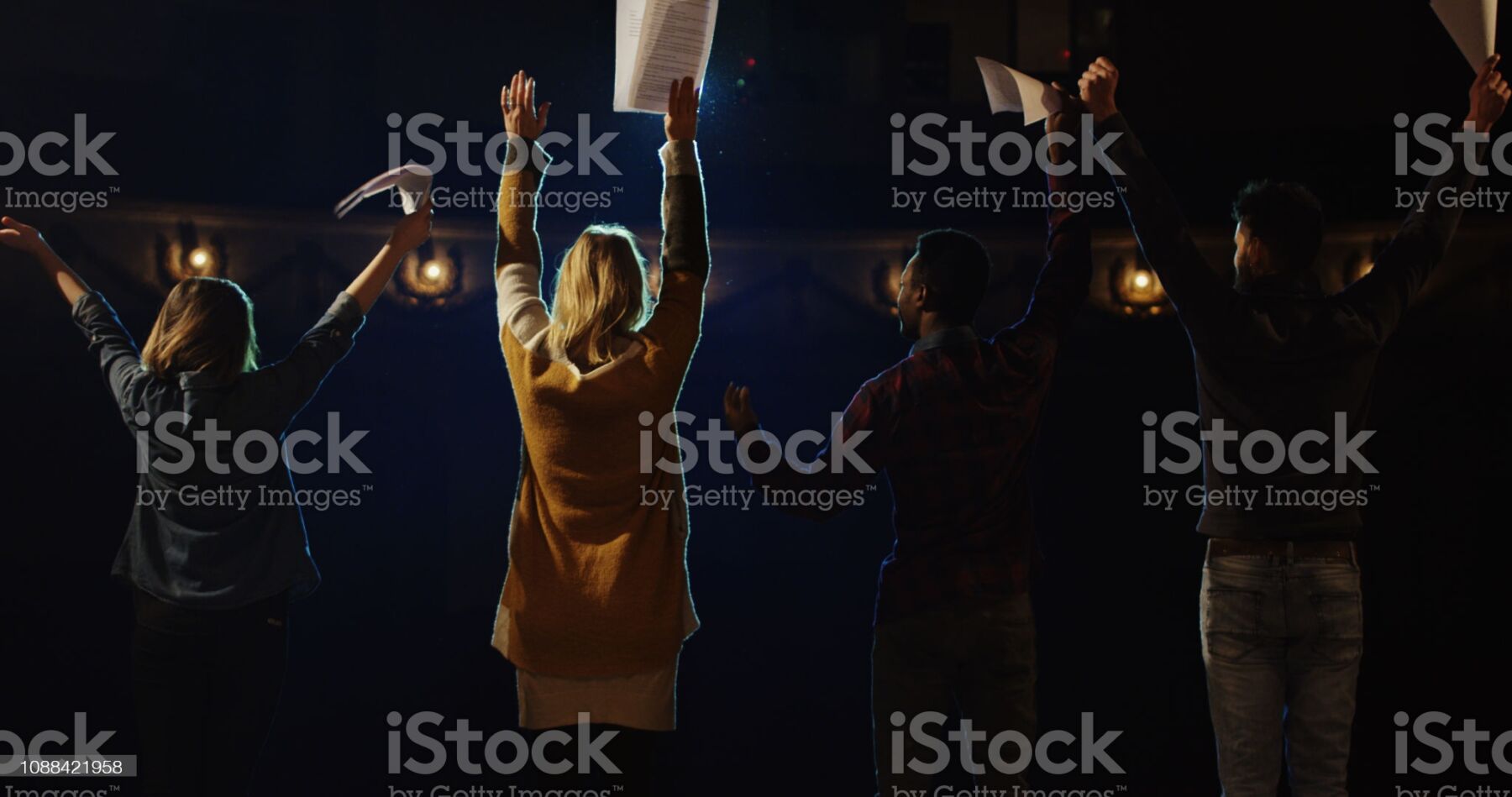 Person raising hand in a dark, moody setting with warm light.