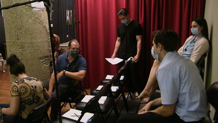 Three men preparing for a scene in a theater setting with scripts.