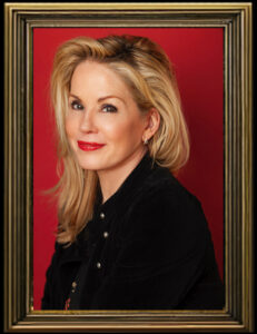 Blonde woman with red lipstick posing confidently against a red and gold background.