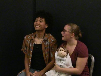 Two friends smiling and sitting against a black background.