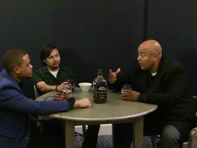 Three men engaged in a discussion around a table.