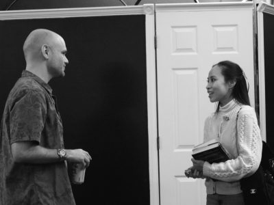 Two people talking indoors, woman holding books