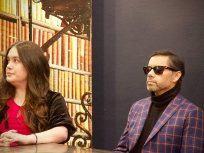 Two panelists at table, man wearing sunglasses